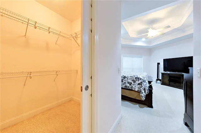 bedroom with light carpet, a raised ceiling, ceiling fan, ornamental molding, and a closet