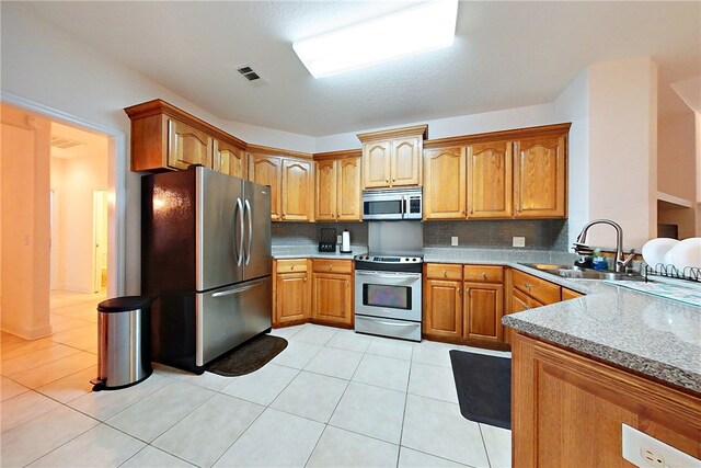 kitchen featuring backsplash, sink, light stone countertops, light tile patterned floors, and appliances with stainless steel finishes