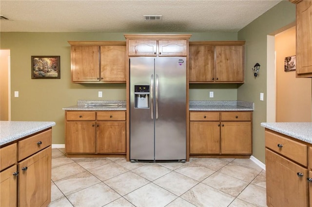1709 Suwanne Dr, Waycross, GA 31501 - kitchen featuring stainless steel fridge with ice dispenser, light countertops, light tile patterned flooring, brown cabinets, and a textured ceiling
