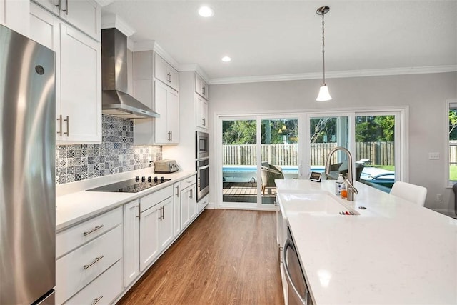 kitchen with appliances with stainless steel finishes, wall chimney exhaust hood, sink, white cabinetry, and hanging light fixtures