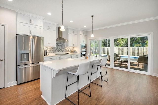 kitchen with stainless steel fridge, a center island with sink, white cabinets, and wall chimney range hood