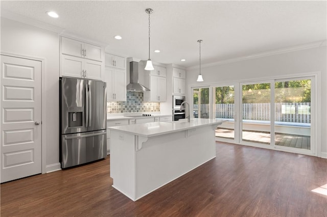 kitchen featuring appliances with stainless steel finishes, white cabinetry, a kitchen island with sink, and wall chimney exhaust hood