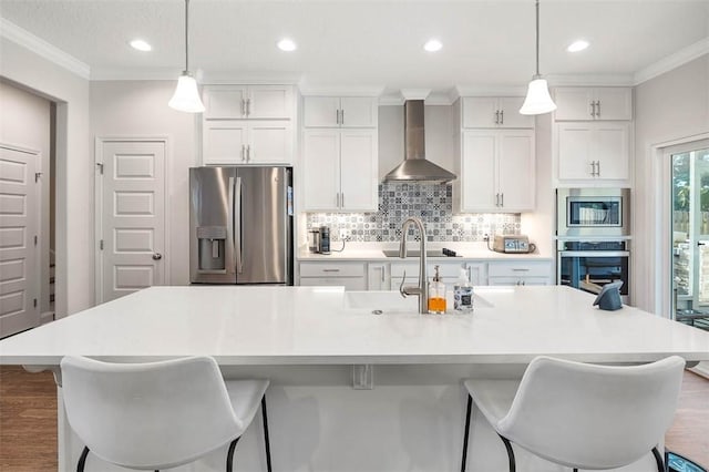 kitchen with stainless steel appliances, hanging light fixtures, wall chimney exhaust hood, and an island with sink