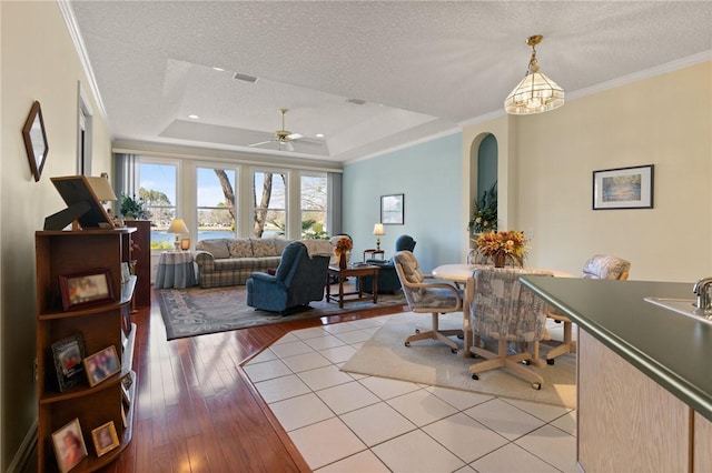 interior space featuring a raised ceiling, ornamental molding, a textured ceiling, and light hardwood / wood-style floors