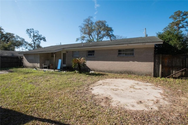 rear view of house featuring fence, brick siding, and a lawn