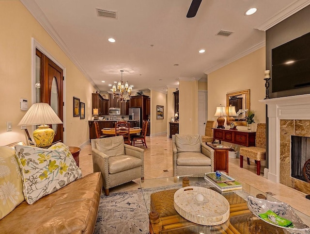 living room featuring a tiled fireplace, crown molding, and ceiling fan with notable chandelier