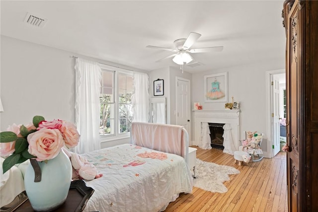 bedroom with a ceiling fan, visible vents, baseboards, a fireplace, and wood-type flooring