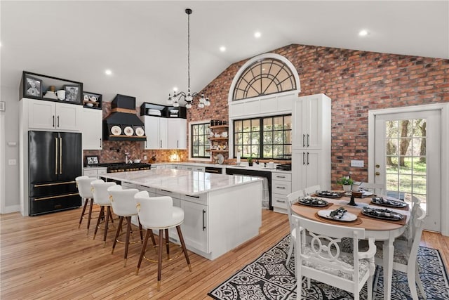 kitchen with light wood-type flooring, custom range hood, a kitchen island, high quality fridge, and white cabinets