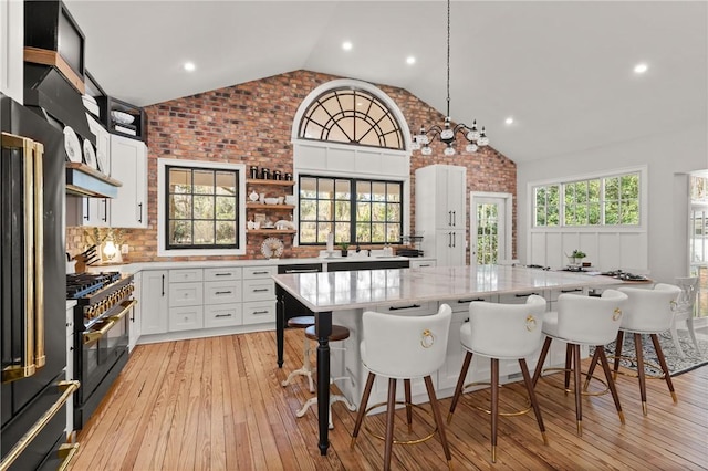 kitchen featuring light wood finished floors, double oven range, a breakfast bar area, white cabinets, and open shelves