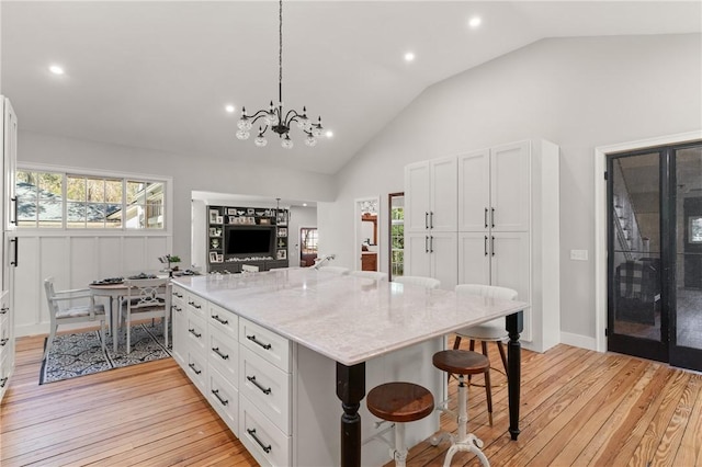 kitchen with light stone countertops, a kitchen bar, lofted ceiling, light wood-style floors, and white cabinets