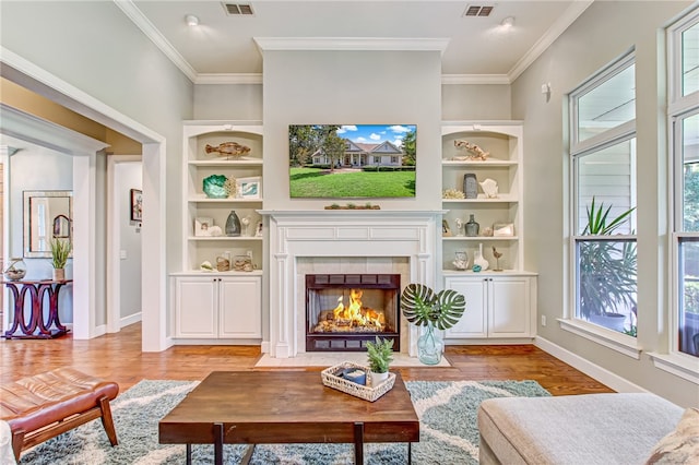 living room with a fireplace, light hardwood / wood-style floors, built in features, and crown molding