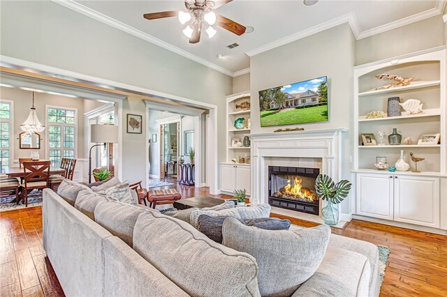 living room featuring light wood-type flooring, ceiling fan, crown molding, and a tiled fireplace