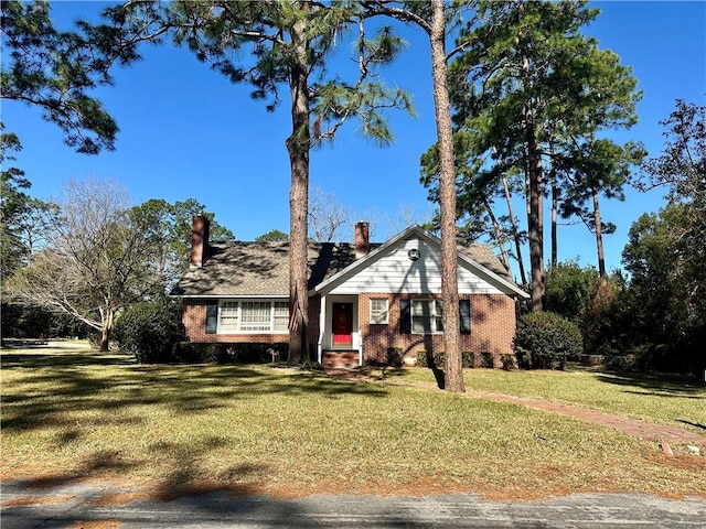 view of front of home with entry steps, a front lawn, a chimney, and brick siding