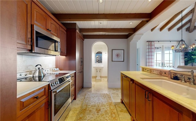 kitchen featuring sink, beamed ceiling, decorative light fixtures, light tile patterned floors, and appliances with stainless steel finishes