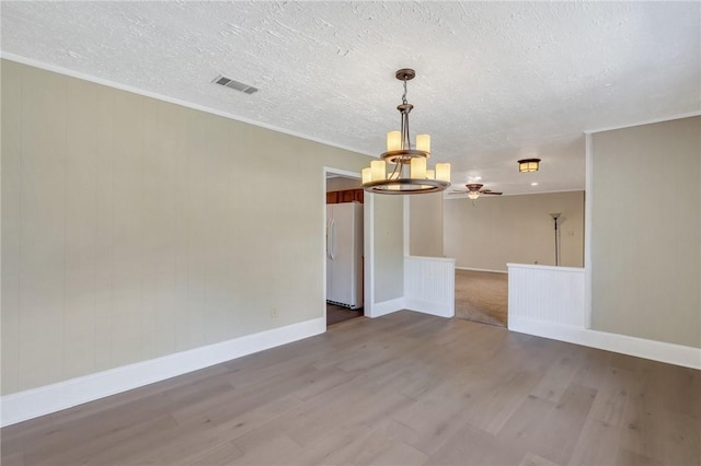 spare room with wood finished floors, baseboards, visible vents, a textured ceiling, and crown molding