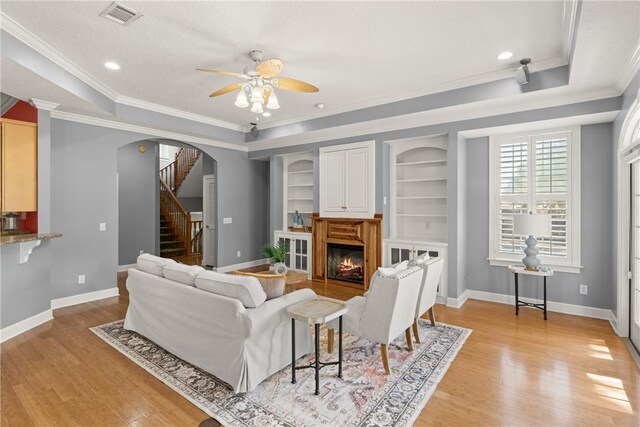 142 Montrose, Saint Simons Island, GA 31522 - living room with a ceiling fan, crown molding, a warm lit fireplace, light wood-style floors, and arched walkways