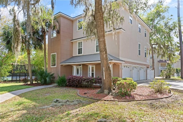 142 Montrose, Saint Simons Island, GA 31522 - view of front of home featuring a garage, concrete driveway, stucco siding, metal roof, and covered porch