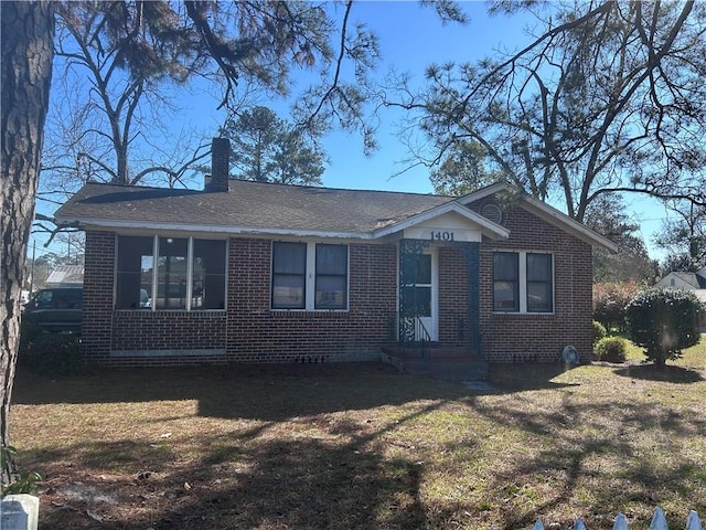 view of front of home with a shingled roof, a chimney, a front lawn, and brick siding