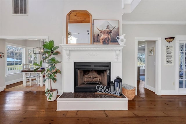 living room featuring visible vents, baseboards, a fireplace with raised hearth, wood-type flooring, and crown molding