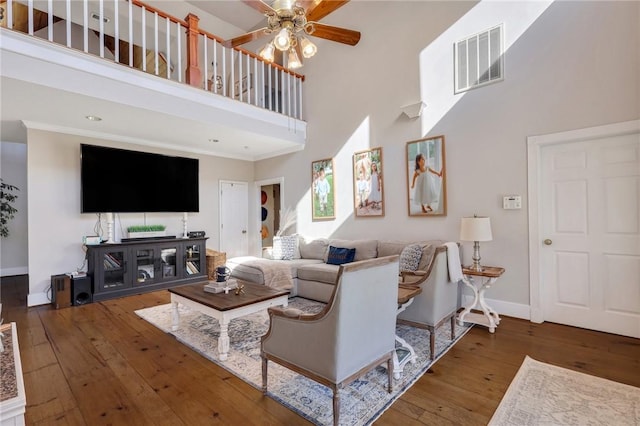 living area featuring visible vents, a towering ceiling, wood-type flooring, baseboards, and ceiling fan