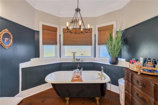 full bath with plenty of natural light, a freestanding bath, an inviting chandelier, and wood finished floors