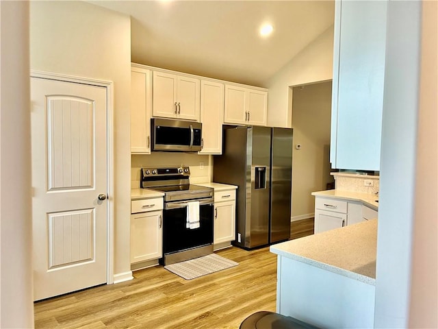 kitchen with lofted ceiling, white cabinets, light wood-style floors, and stainless steel appliances