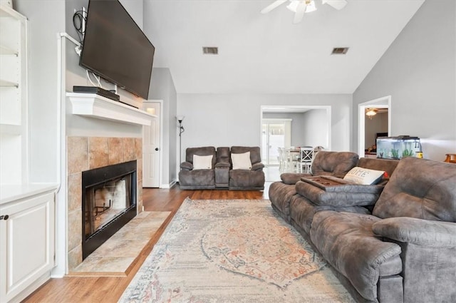 living room featuring lofted ceiling, a tiled fireplace, ceiling fan, and light wood-type flooring