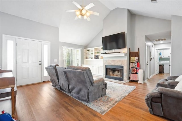 living room with a tiled fireplace, wood-type flooring, high vaulted ceiling, and ceiling fan