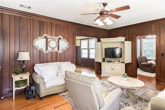 living room with a ceiling fan, wooden walls, a healthy amount of sunlight, and visible vents