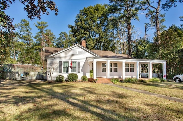 view of front of home with a porch, fence, a chimney, and a front yard