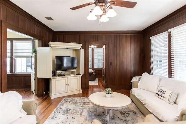 living room featuring ornamental molding, wood walls, ceiling fan, and visible vents