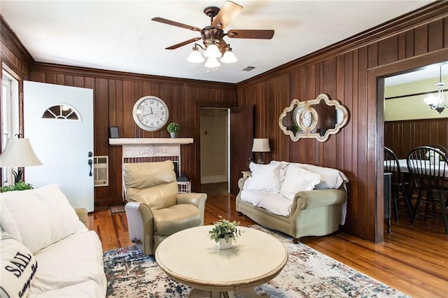 living room with ceiling fan, wood walls, and crown molding