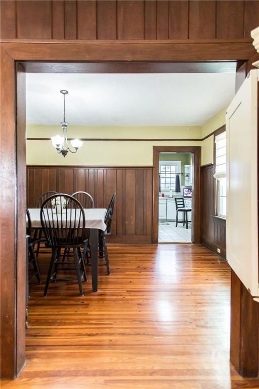 dining space featuring a wainscoted wall, light wood-style flooring, a notable chandelier, and wooden walls