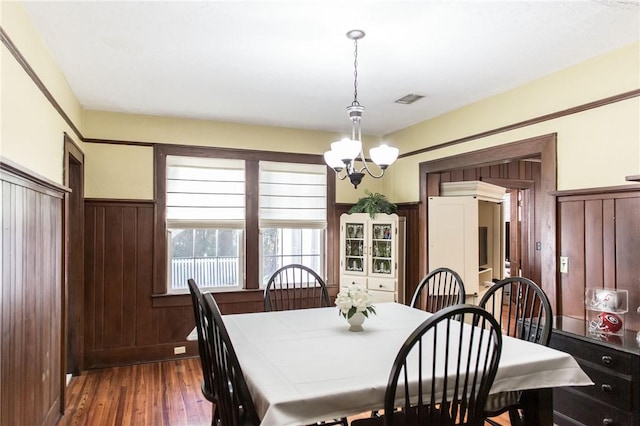 dining room with wood finished floors, visible vents, wooden walls, wainscoting, and a notable chandelier