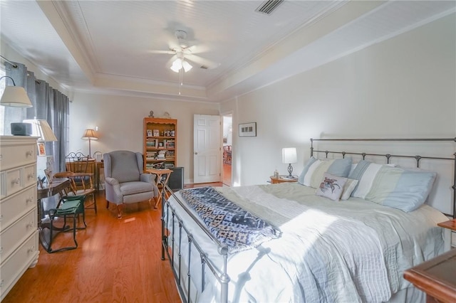 bedroom with a tray ceiling, ornamental molding, visible vents, and light wood-type flooring