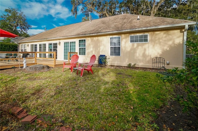 back of property featuring a deck, a yard, a shingled roof, and stucco siding