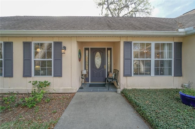 doorway to property featuring stucco siding and roof with shingles