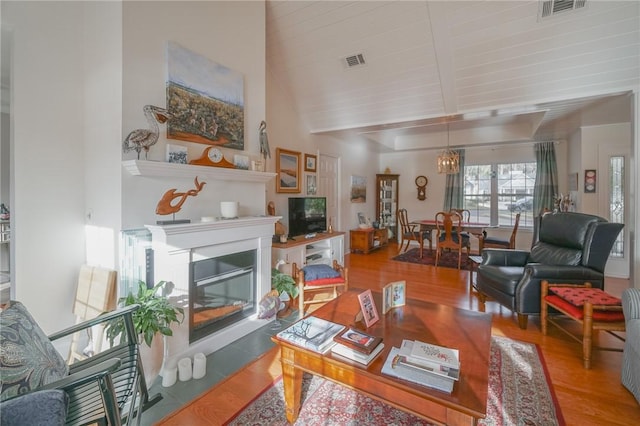 living area with visible vents, beamed ceiling, a glass covered fireplace, and wood finished floors