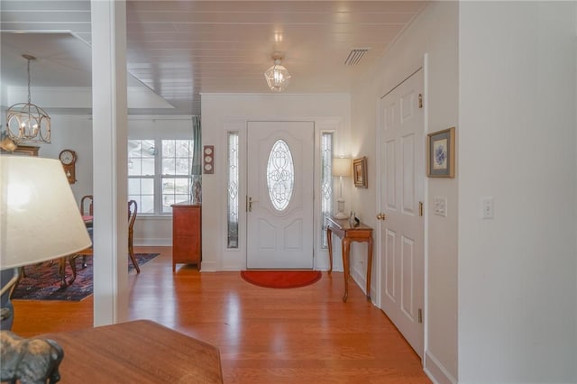 foyer entrance featuring visible vents, ornamental molding, wood finished floors, an inviting chandelier, and baseboards