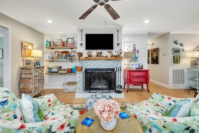 living area featuring a fireplace, wood finished floors, a ceiling fan, and crown molding