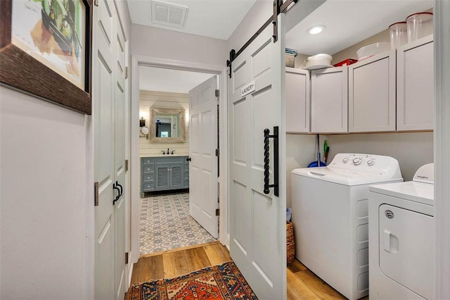 washroom with cabinet space, a barn door, visible vents, washing machine and clothes dryer, and light wood-style floors