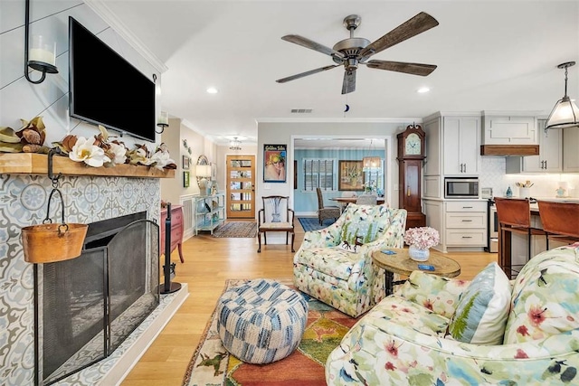 living area featuring ceiling fan, a fireplace, visible vents, light wood-style floors, and ornamental molding