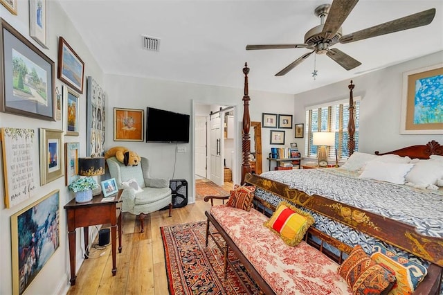 bedroom with light wood-style floors, a barn door, visible vents, and ceiling fan