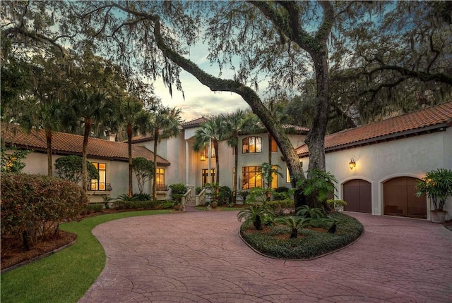 mediterranean / spanish-style home featuring a tile roof, curved driveway, and stucco siding