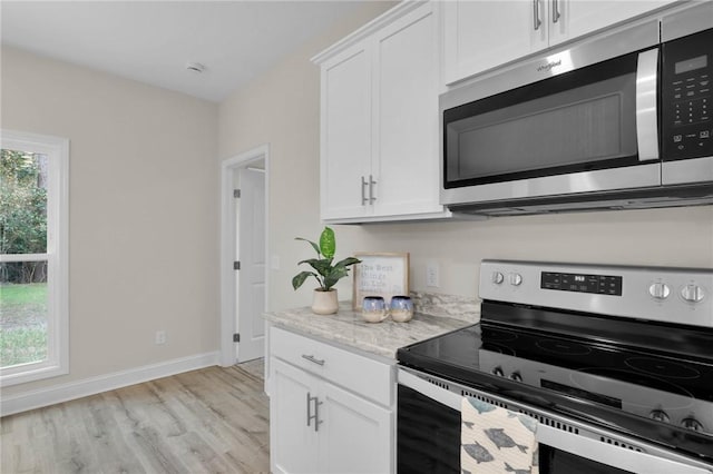 kitchen featuring light stone countertops, light wood-type flooring, stainless steel appliances, and white cabinetry