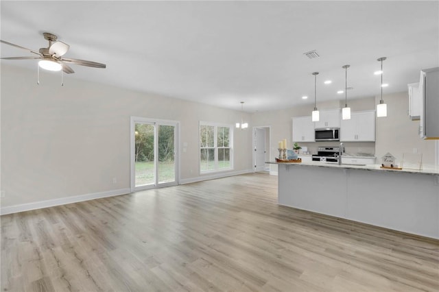 kitchen featuring white cabinetry, light wood-type flooring, decorative light fixtures, and appliances with stainless steel finishes