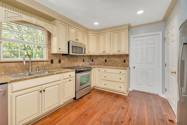 212 Stillwater Dr, Brunswick, GA 31525 - kitchen featuring cream cabinetry, a sink, light wood-style floors, decorative backsplash, and appliances with stainless steel finishes