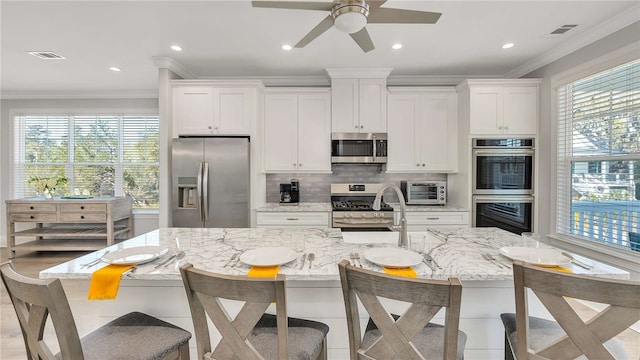 kitchen with white cabinets, light stone countertops, stainless steel appliances, and an island with sink