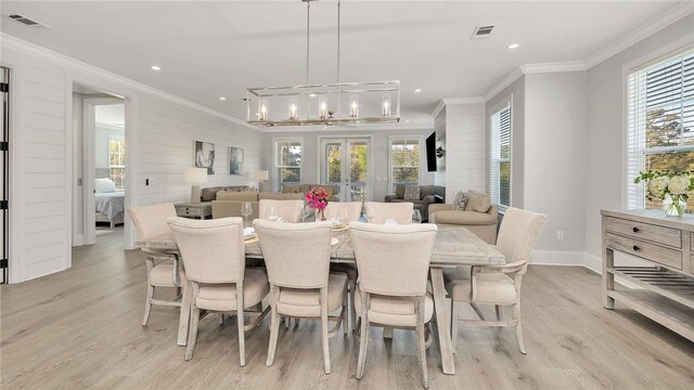 dining space with a notable chandelier, light wood-type flooring, ornamental molding, and wooden walls