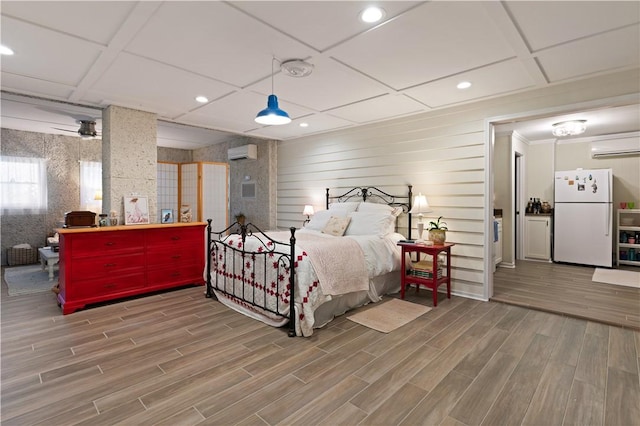bedroom with wood finished floors, freestanding refrigerator, a wall unit AC, and recessed lighting